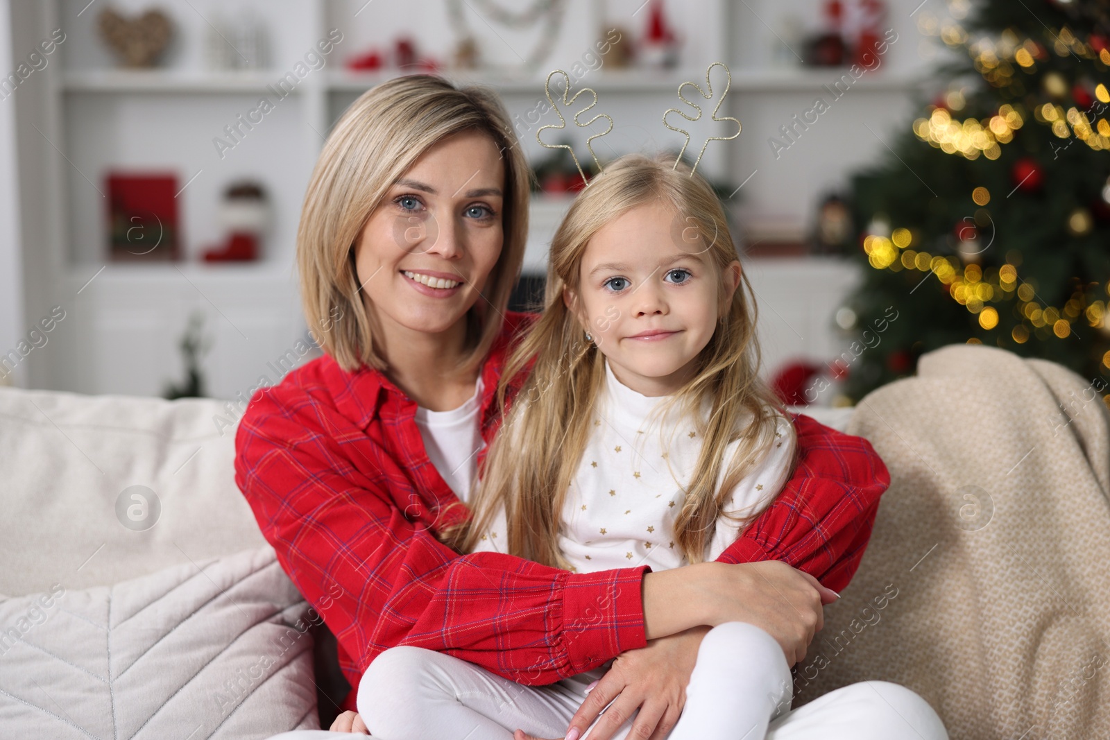 Photo of Cute little girl with her mom on sofa against Christmas lights