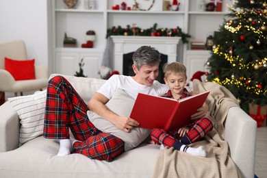 Father and son reading book together on sofa at home. Christmas holidays