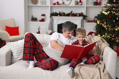 Father and son reading book together on sofa at home. Christmas holidays