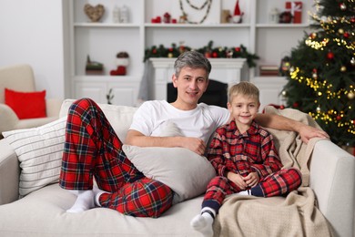 Father and son in pajamas on sofa at home. Christmas morning