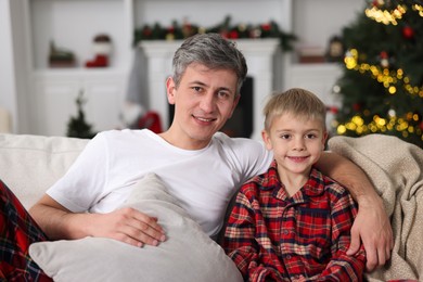 Father and son in pajamas on sofa at home. Christmas morning