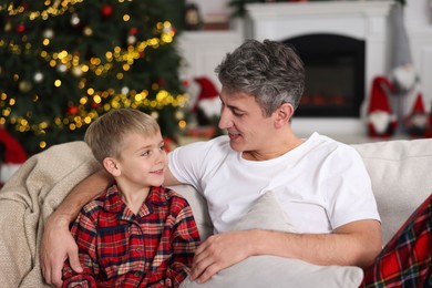 Father and son in pajamas on sofa at home. Christmas morning