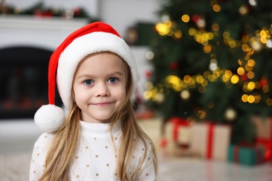 Portrait of cute little girl in Santa hat against Christmas lights