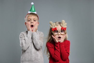 Funny children in Christmas accessories on grey background