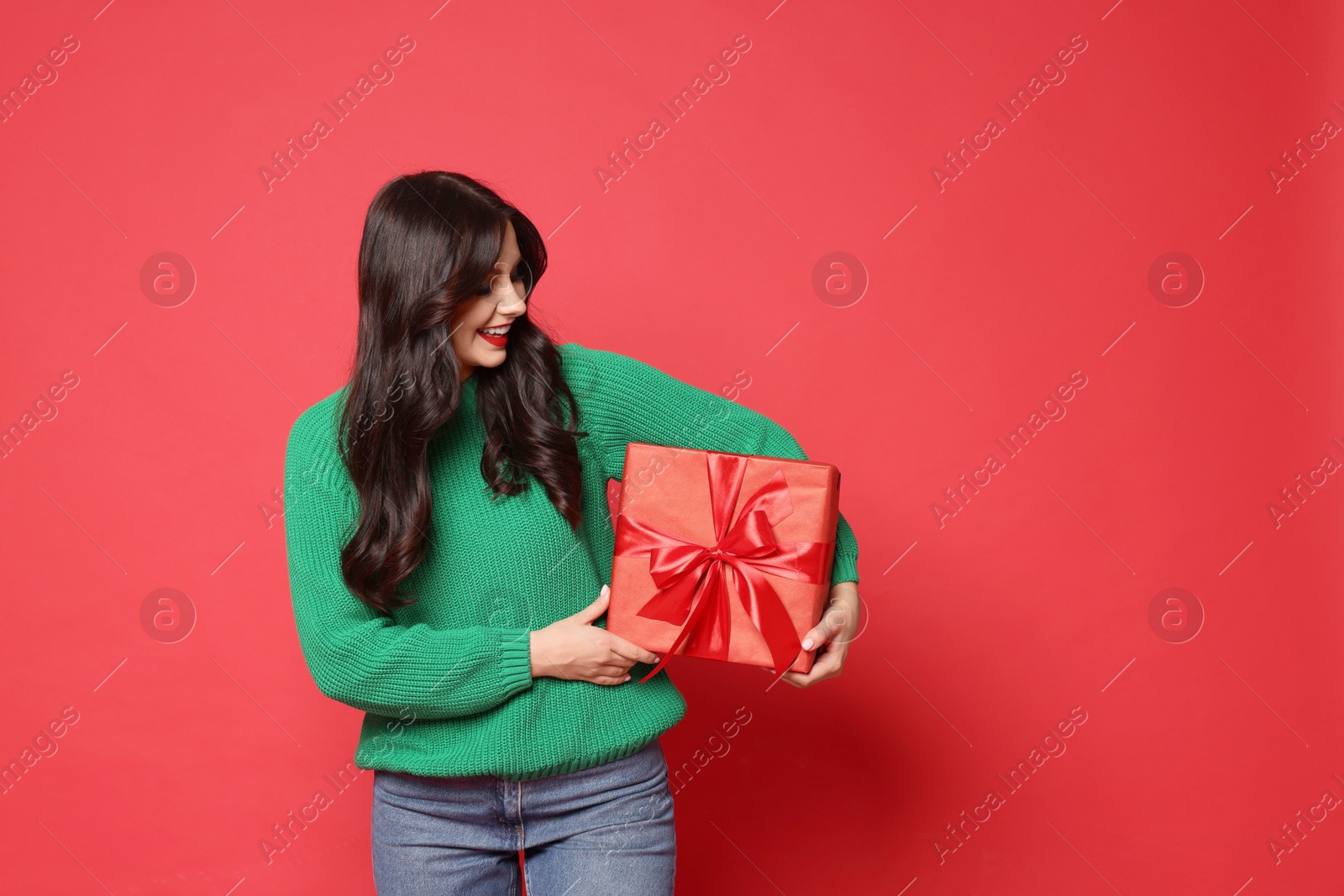 Photo of Happy woman with Christmas present on red background, space for text