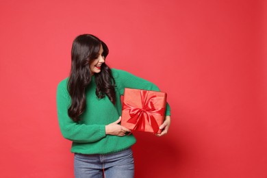 Photo of Happy woman with Christmas present on red background, space for text