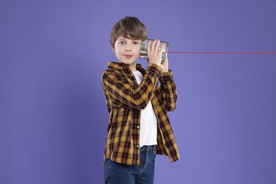 Boy using tin can telephone on violet background