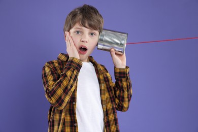 Photo of Boy using tin can telephone on violet background