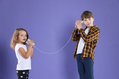 Photo of Boy and girl talking on tin can telephone against violet background