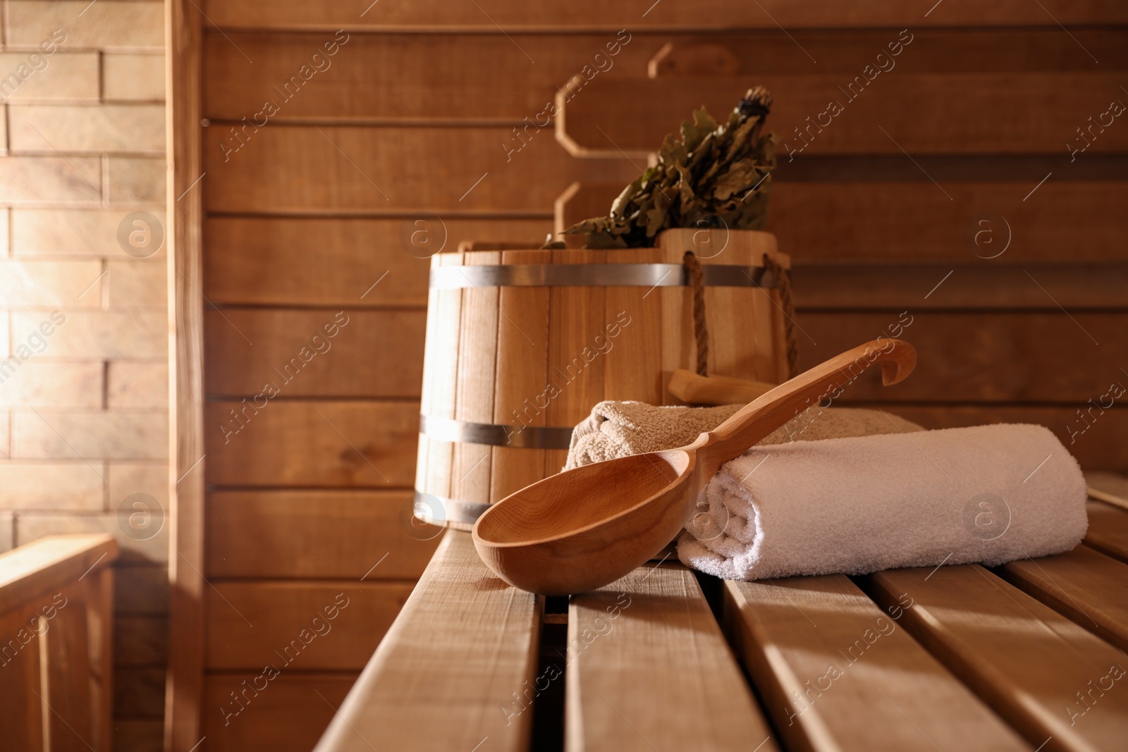 Photo of Ladle, towels, bucket and whisk on wooden bench in sauna. Space for text