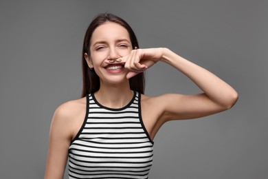 Happy woman holding finger with drawn mustache above lips on grey background