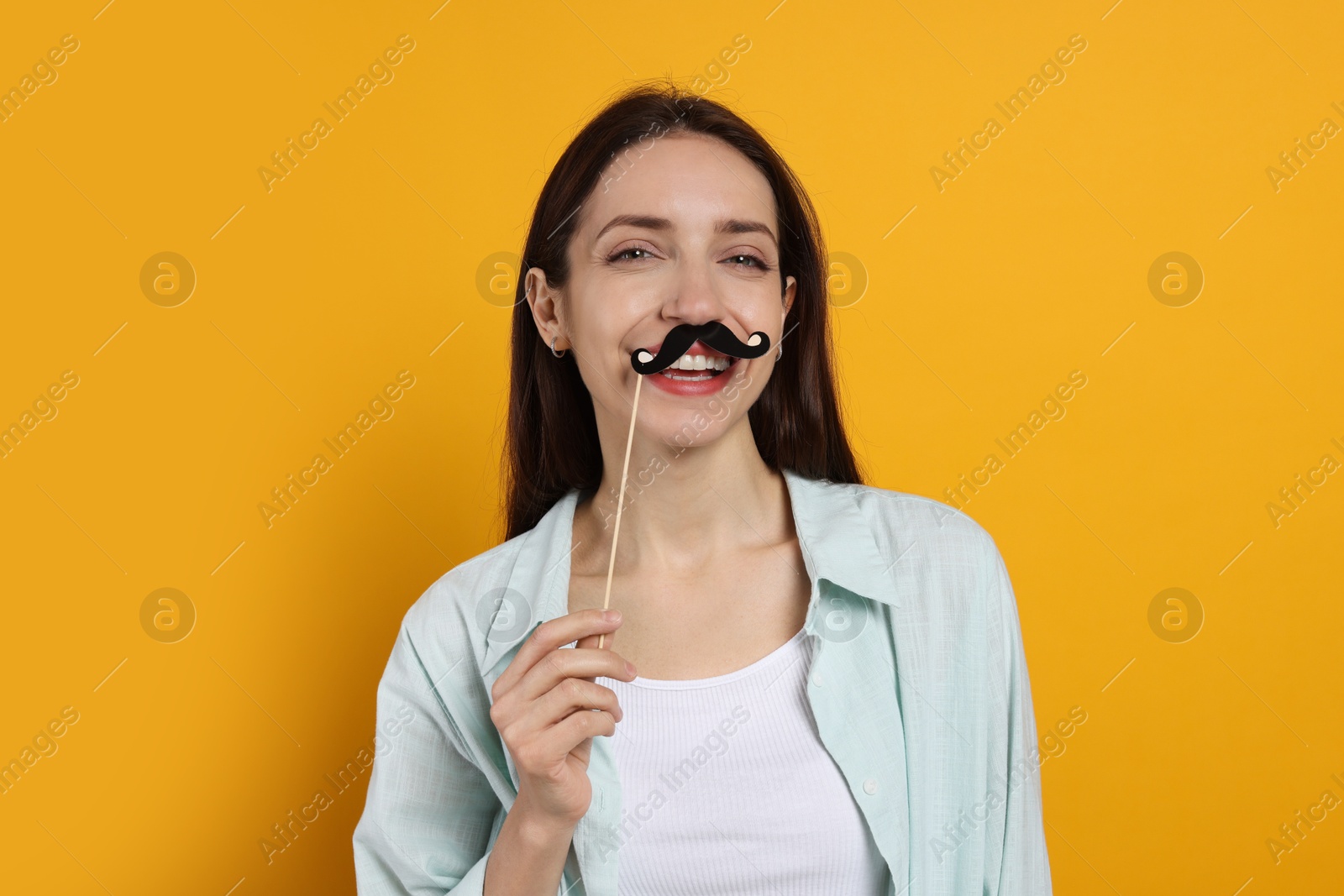 Photo of Happy woman with fake paper mustache on orange background