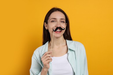 Happy woman with fake paper mustache on orange background