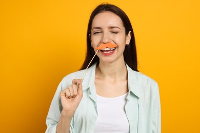 Photo of Happy woman with fake paper mustache on orange background