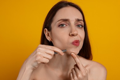 Beautiful woman plucking her facial hair with tweezers on orange background