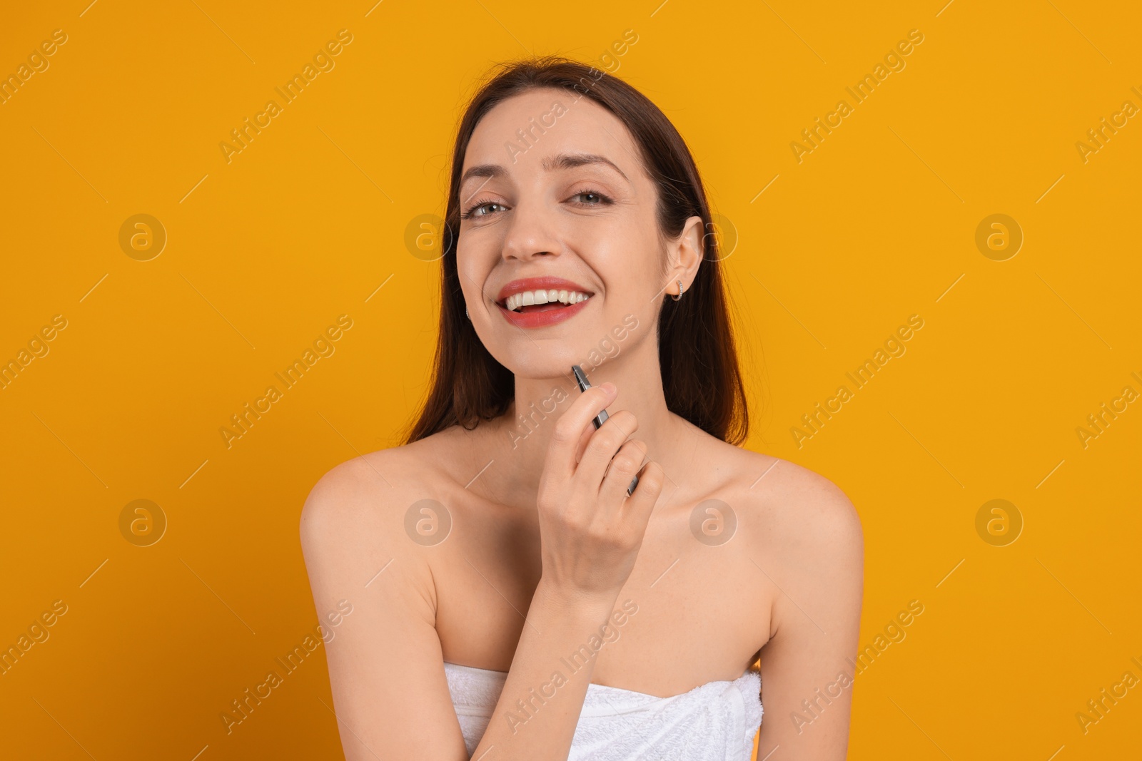 Photo of Happy woman plucking her facial hair with tweezers on orange background