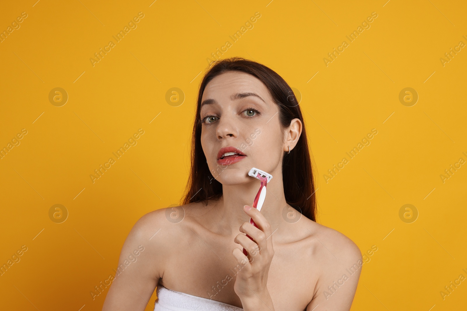 Photo of Beautiful woman shaving her facial hair with razor on orange background