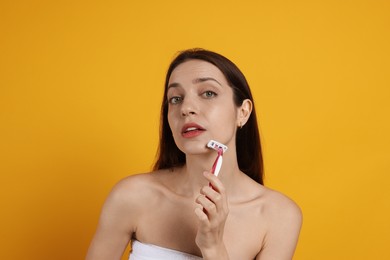 Photo of Beautiful woman shaving her facial hair with razor on orange background