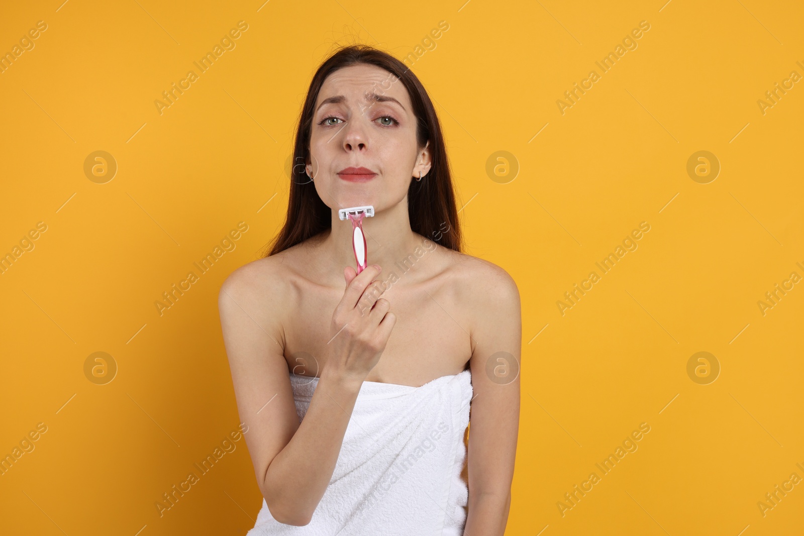 Photo of Beautiful woman shaving her facial hair with razor on orange background