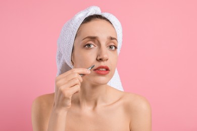 Photo of Beautiful woman plucking her mustache with tweezers on pink background