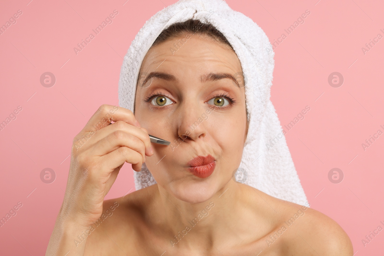 Photo of Beautiful woman plucking her facial hair with tweezers on pink background