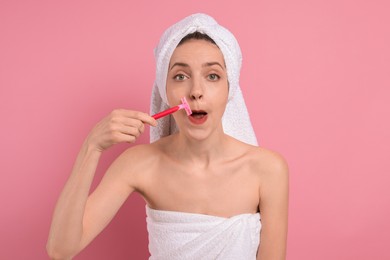 Beautiful woman shaving her mustache with razor on pink background