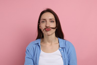 Funny woman making mustache from her hair on pink background