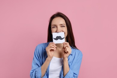 Woman holding paper with drawn mustache on pink background