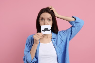 Woman holding paper with drawn mustache on pink background