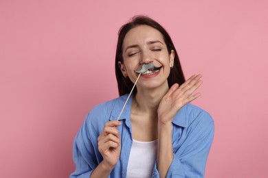 Happy woman with fake paper mustache on pink background