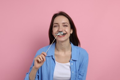 Happy woman with fake paper mustache on pink background