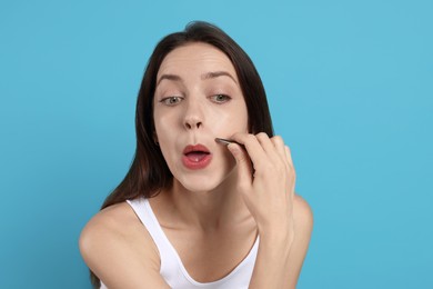 Photo of Woman plucking her mustache with tweezers on light blue background