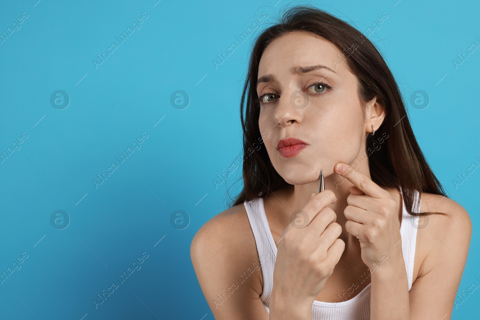 Photo of Woman plucking her facial hair with tweezers on light blue background. Space for text