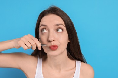 Photo of Woman plucking her mustache with tweezers on light blue background