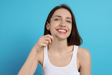 Happy woman plucking her facial hair with tweezers on light blue background