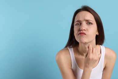 Woman plucking her facial hair with tweezers on light blue background. Space for text