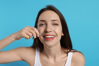 Happy woman plucking her mustache with tweezers on light blue background