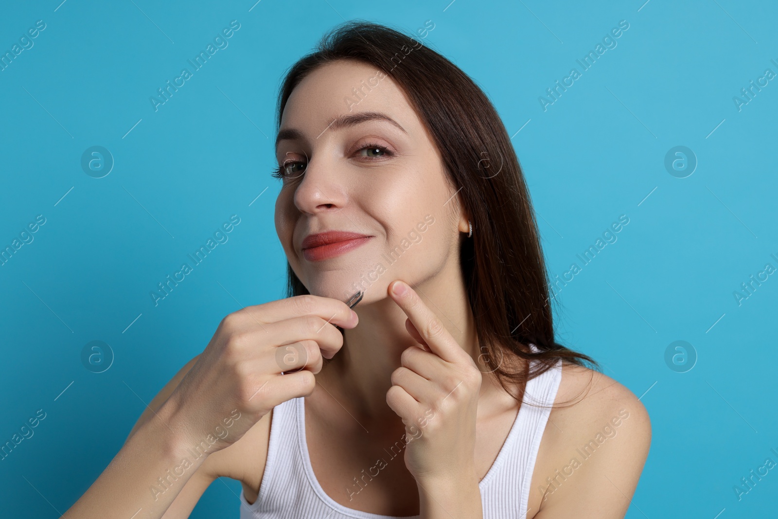 Photo of Woman plucking her facial hair with tweezers on light blue background