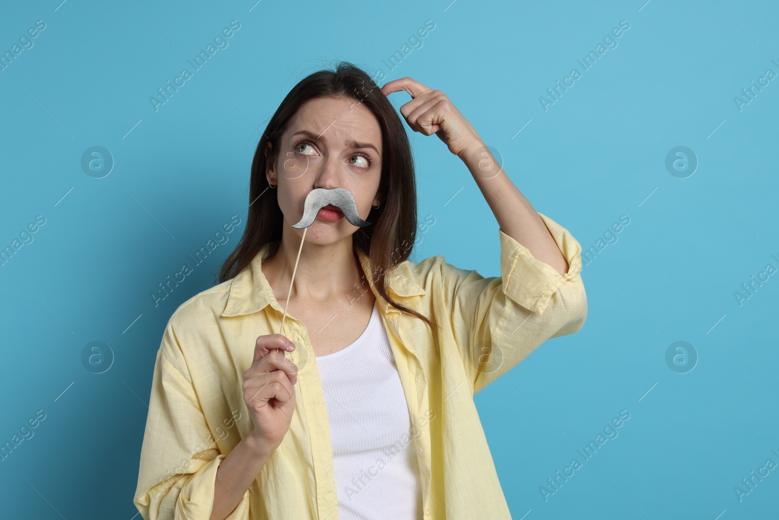 Photo of Thoughtful woman with fake paper mustache on light blue background