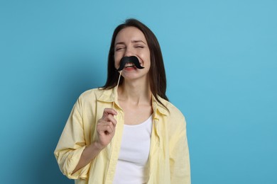 Happy woman with fake paper mustache on light blue background