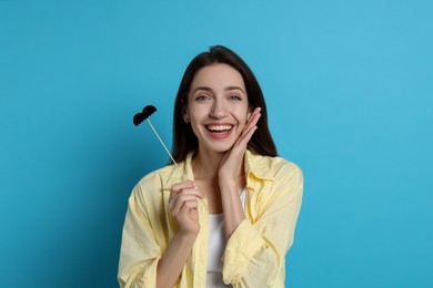 Happy woman with fake paper mustache on light blue background