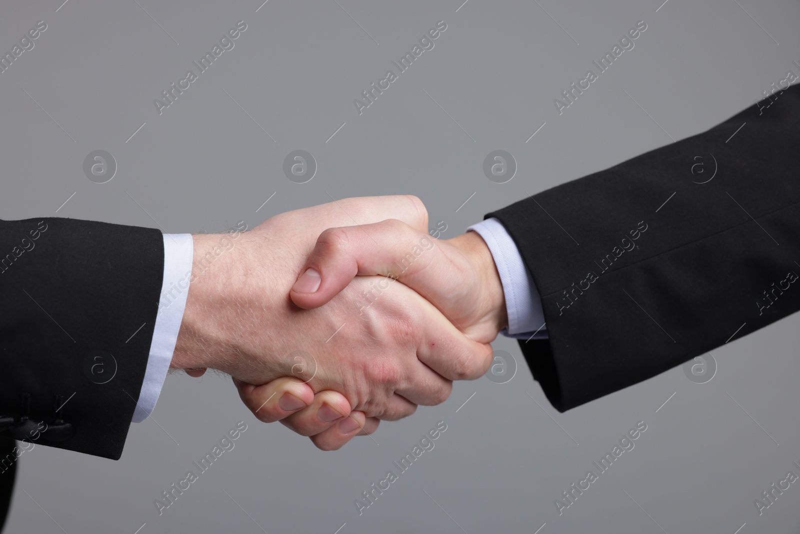 Photo of Businessmen shaking hands on grey background, closeup