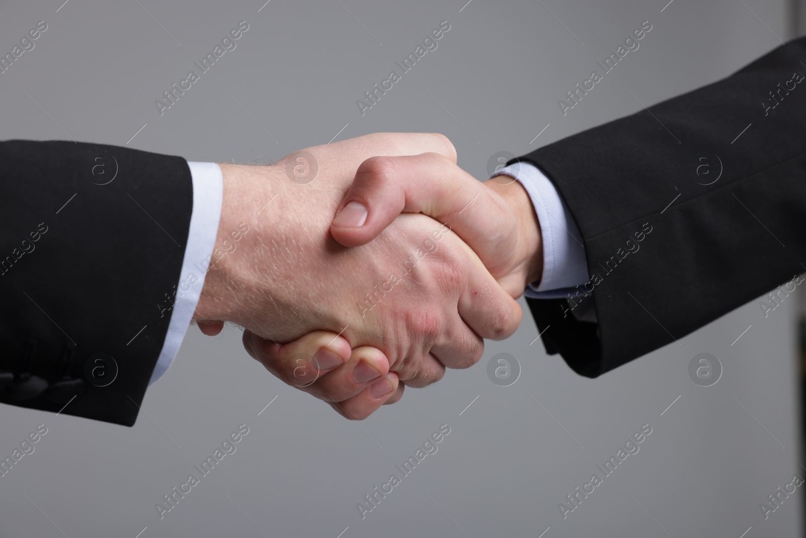 Photo of Businessmen shaking hands on grey background, closeup