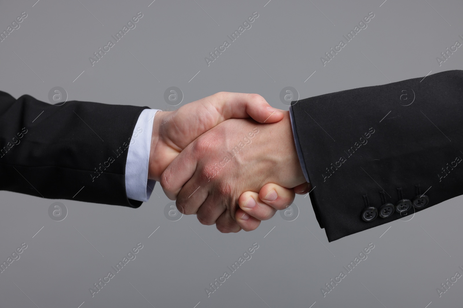 Photo of Businessmen shaking hands on grey background, closeup