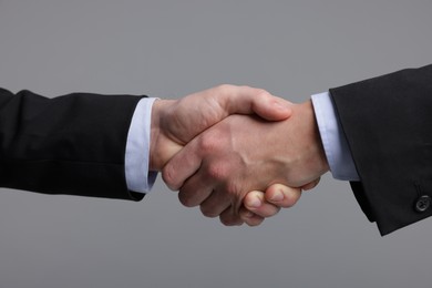 Photo of Businessmen shaking hands on grey background, closeup