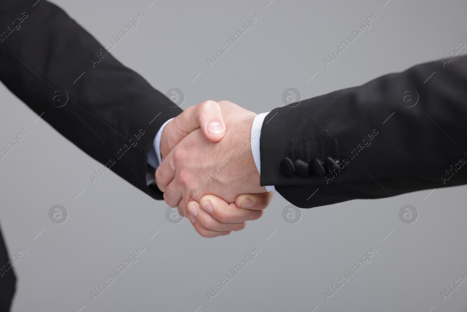 Photo of Businessmen shaking hands on grey background, closeup