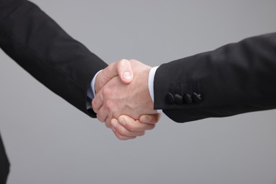 Photo of Businessmen shaking hands on grey background, closeup