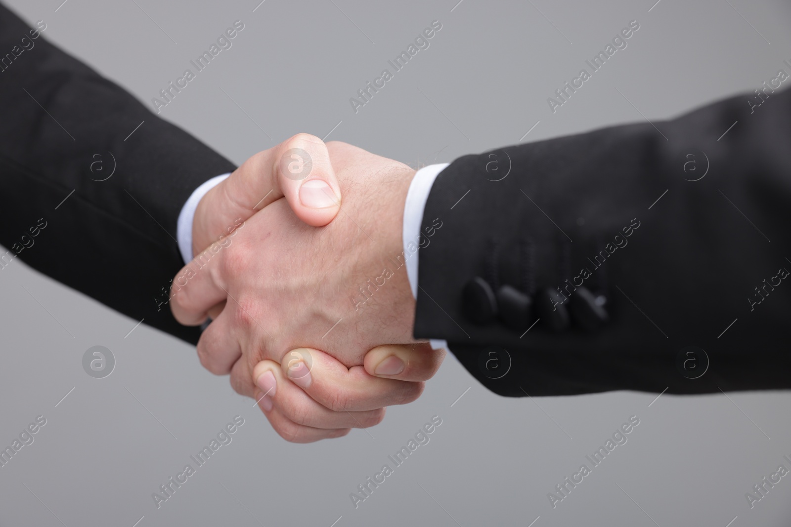 Photo of Businessmen shaking hands on grey background, closeup