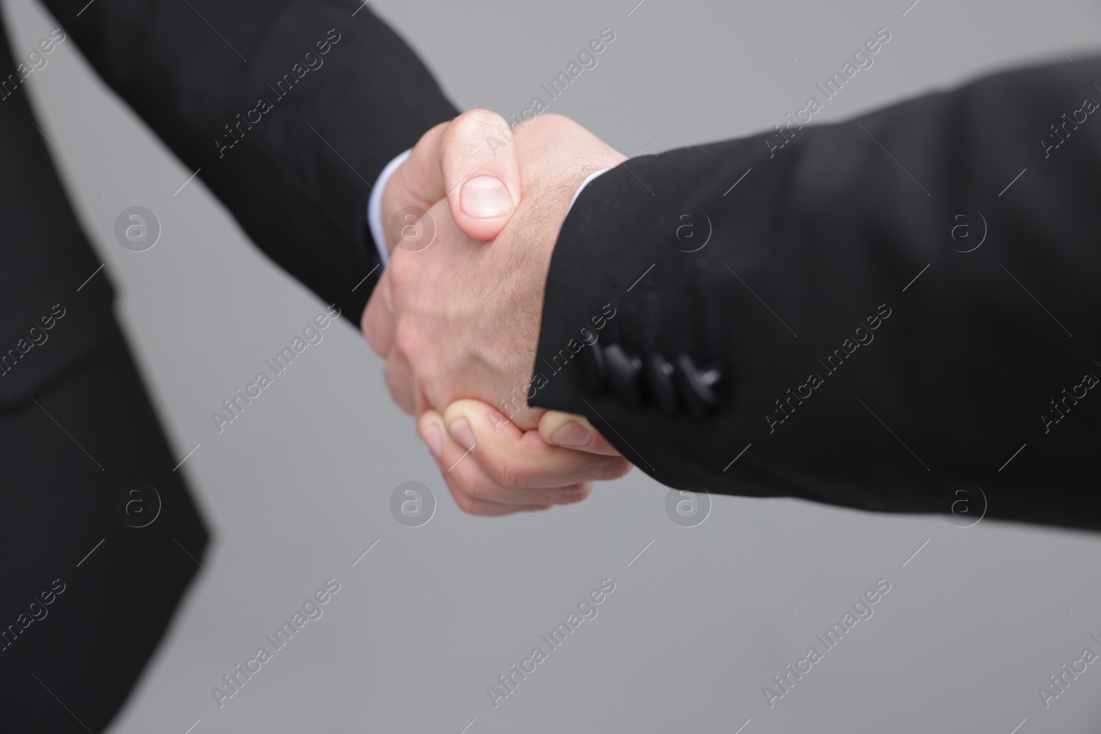 Photo of Businessmen shaking hands on grey background, closeup