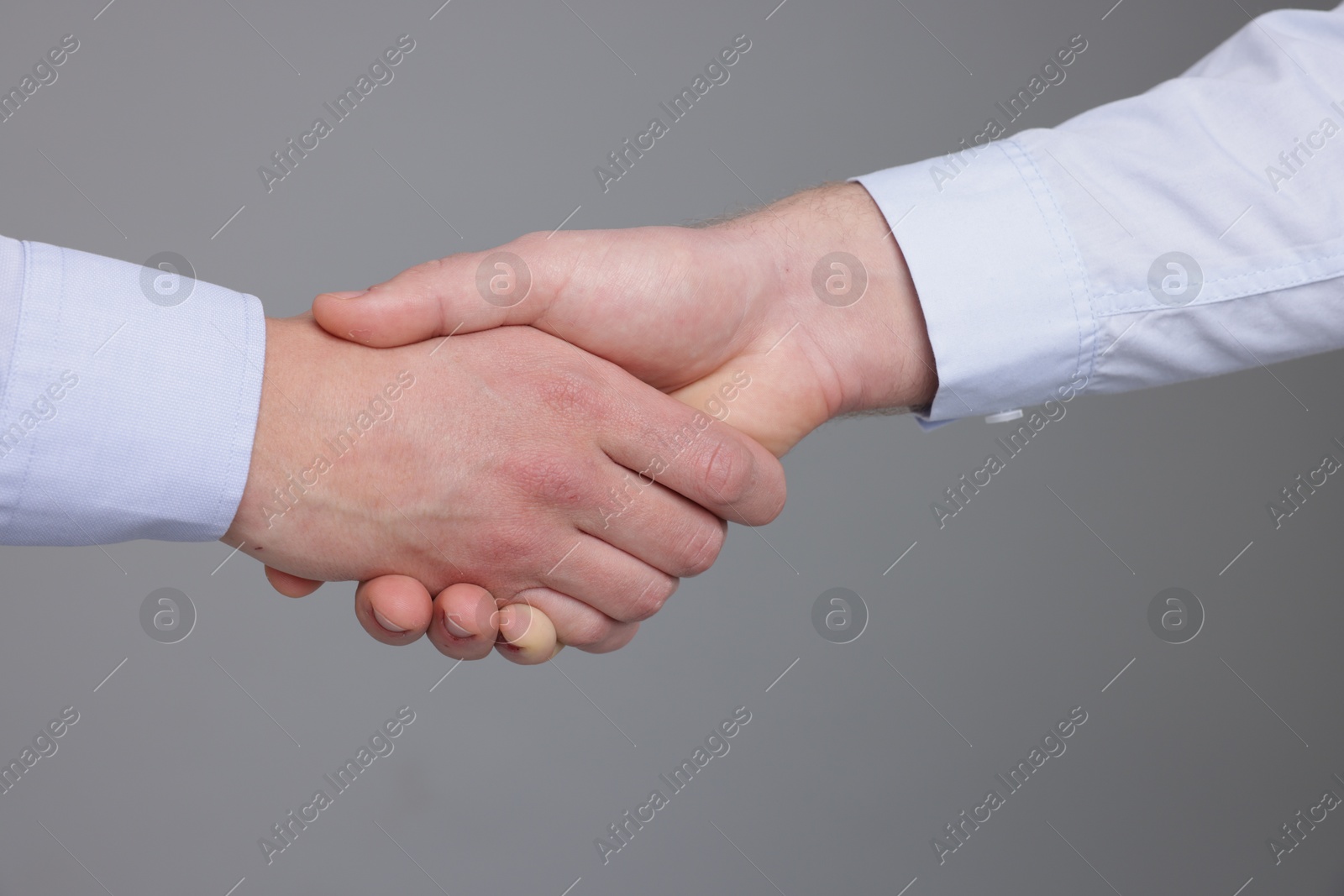 Photo of Businessmen shaking hands on grey background, closeup